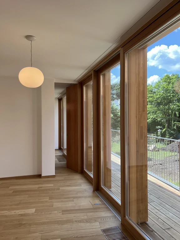 Jasny pokój z drewnianą podłogą i pasem wysokich okien przy tarasie